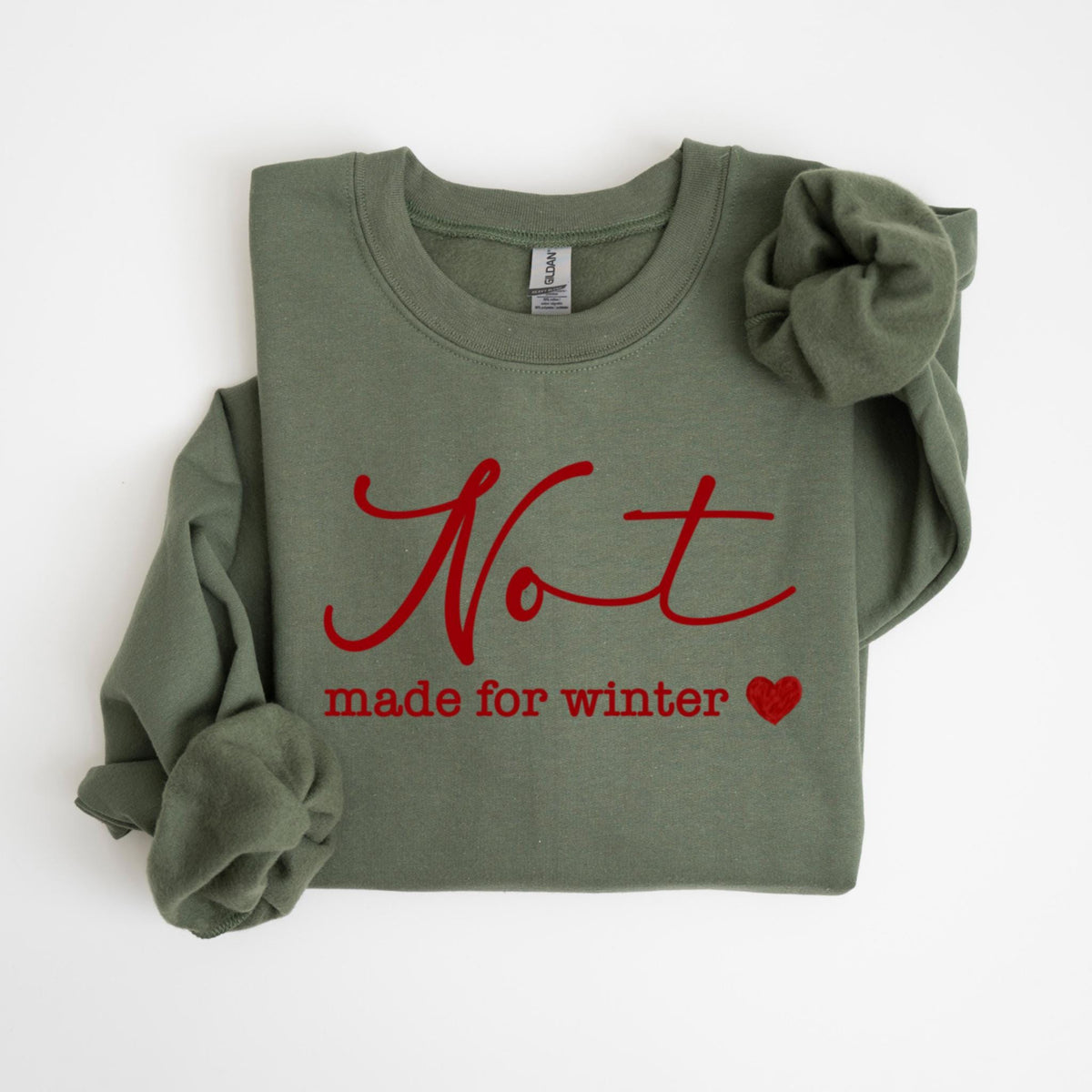 May include: An olive green sweatshirt with the red text "Not made for winter" and a red heart. The long-sleeved crew neck top is folded, with one sleeve visible.