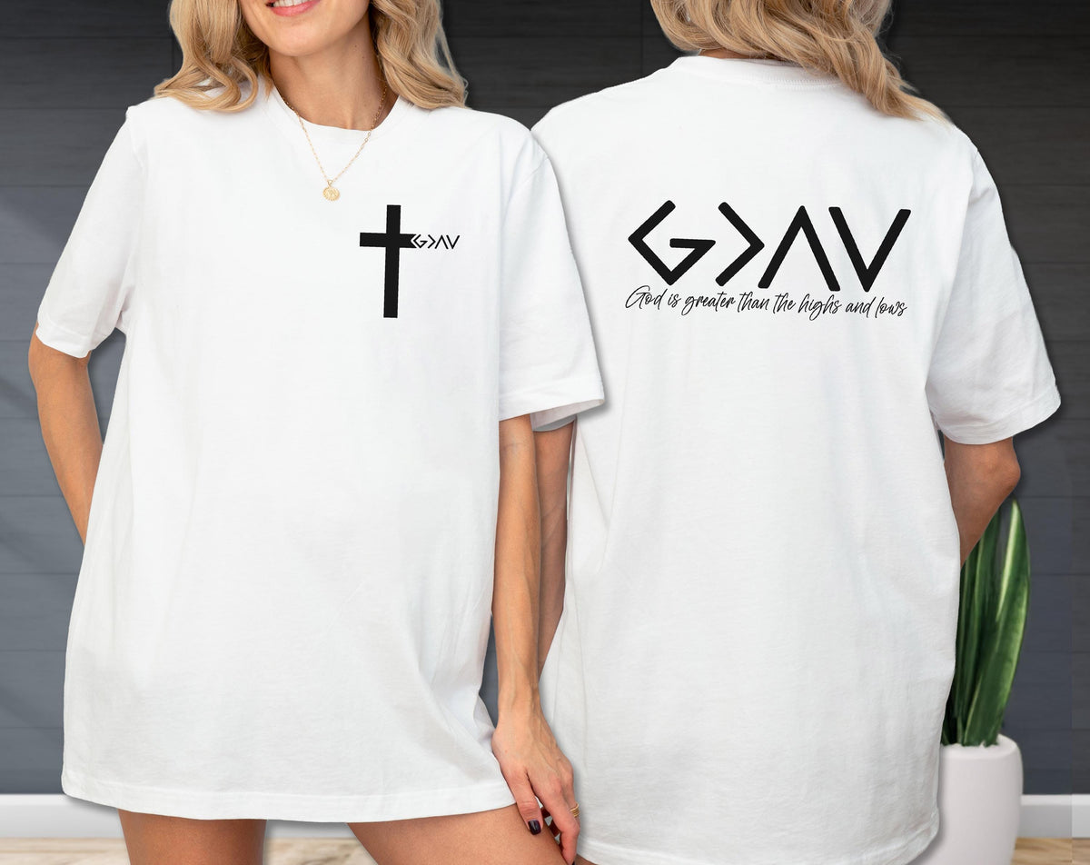 May include: White t-shirt with a black cross and the text "G>AV" on the front. The back of the shirt features the text "G>AV" above the phrase "God is greater than the highs and lows" in black. The shirt is a casual, everyday wear item.
