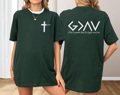 May include: Dark green t-shirt with a white cross and the letters "G>AV" printed on the front. The back of the shirt features the text "G>AV" above the phrase "God is greater than the highs and lows" in white.