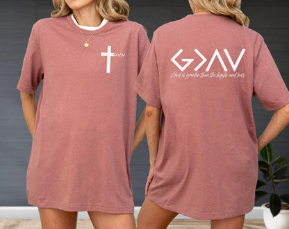 May include: A dusty rose t-shirt with a white cross graphic on the front and the text "God is greater than the highs and lows" on the back. The shirt has a white collar.