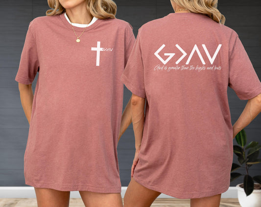 May include: A dusty rose t-shirt with a white cross graphic on the front and the text "God is greater than the highs and lows" on the back. The shirt has a white collar.