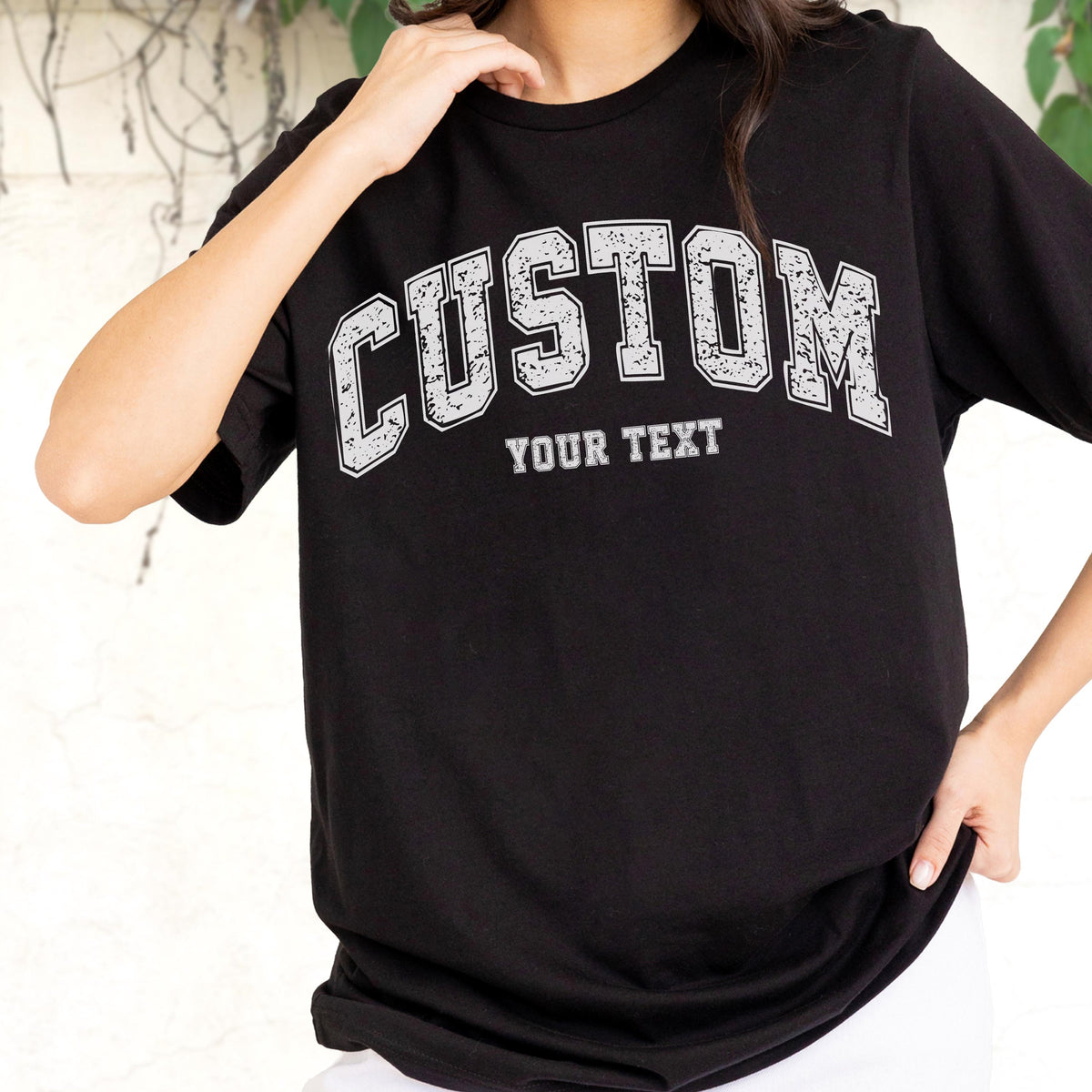 May include: Black t-shirt with the word "CUSTOM" in distressed white block letters arched across the chest. Below the word "CUSTOM" is the text "YOUR TEXT" in a smaller, similar font. The shirt is a classic crew neck style.