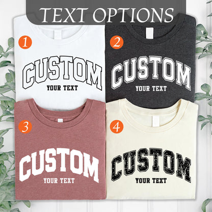 May include: Four t-shirts in white, charcoal, mauve, and cream, each with a custom design. The word "CUSTOM" is arched across the front in a bold, collegiate-style font, with the words "YOUR TEXT" below.