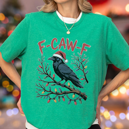 May include: A bright green short-sleeve t-shirt featuring a graphic of a black crow wearing a red and white Santa hat perched on a branch wrapped in colorful Christmas lights. The text F-CAW-F is printed in red above the crow illustration.