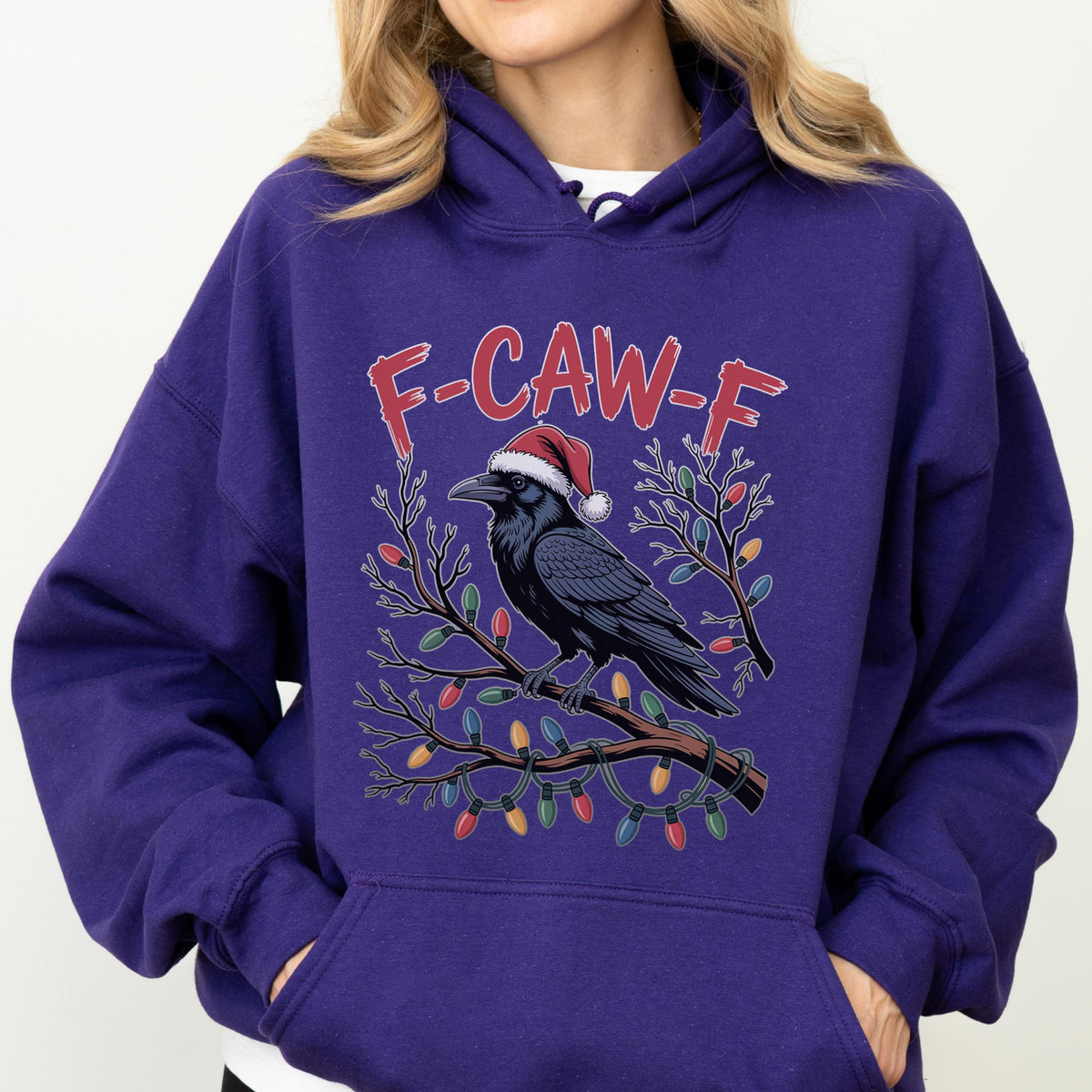 May include: A deep purple hooded sweatshirt featuring a graphic of a black raven wearing a red and white Santa hat, perched on a brown branch wrapped in colorful Christmas lights, with the red text F-CAW-F printed above the bird.
