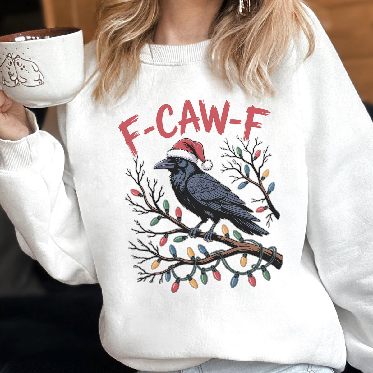 May include: A white crewneck sweatshirt featuring a graphic of a black raven wearing a red and white Santa hat, perched on a bare tree branch wrapped in colorful Christmas lights, with the red text F-CAW-F printed above the bird illustration.