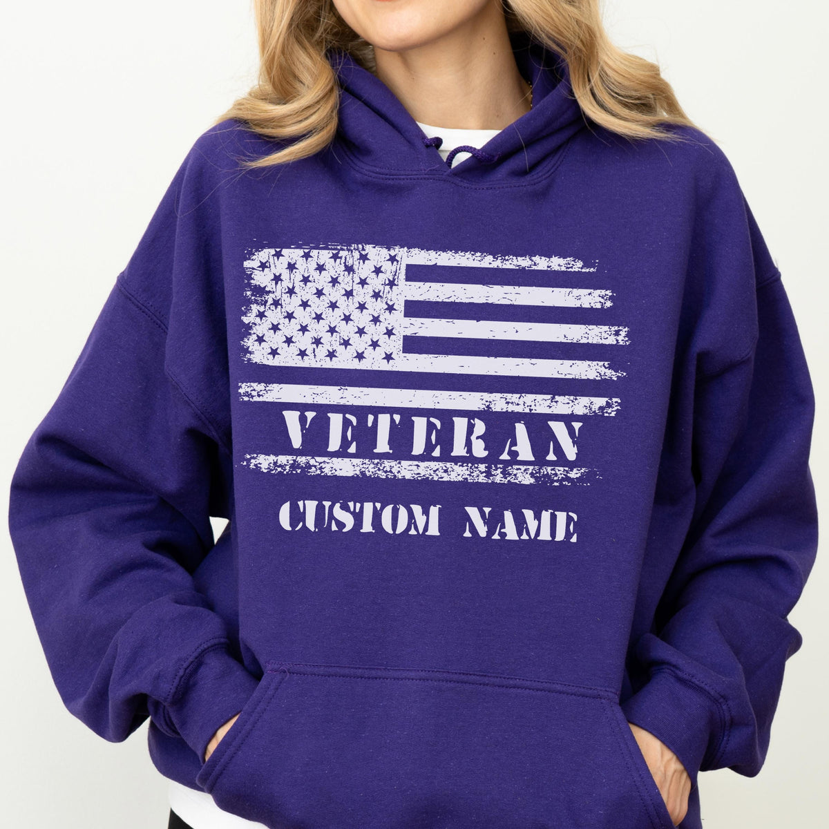 May include: A purple hoodie with a white distressed American flag design. The text "VETERAN" and "CUSTOM NAME" are printed below the flag. The hoodie has a hood and a front pocket.