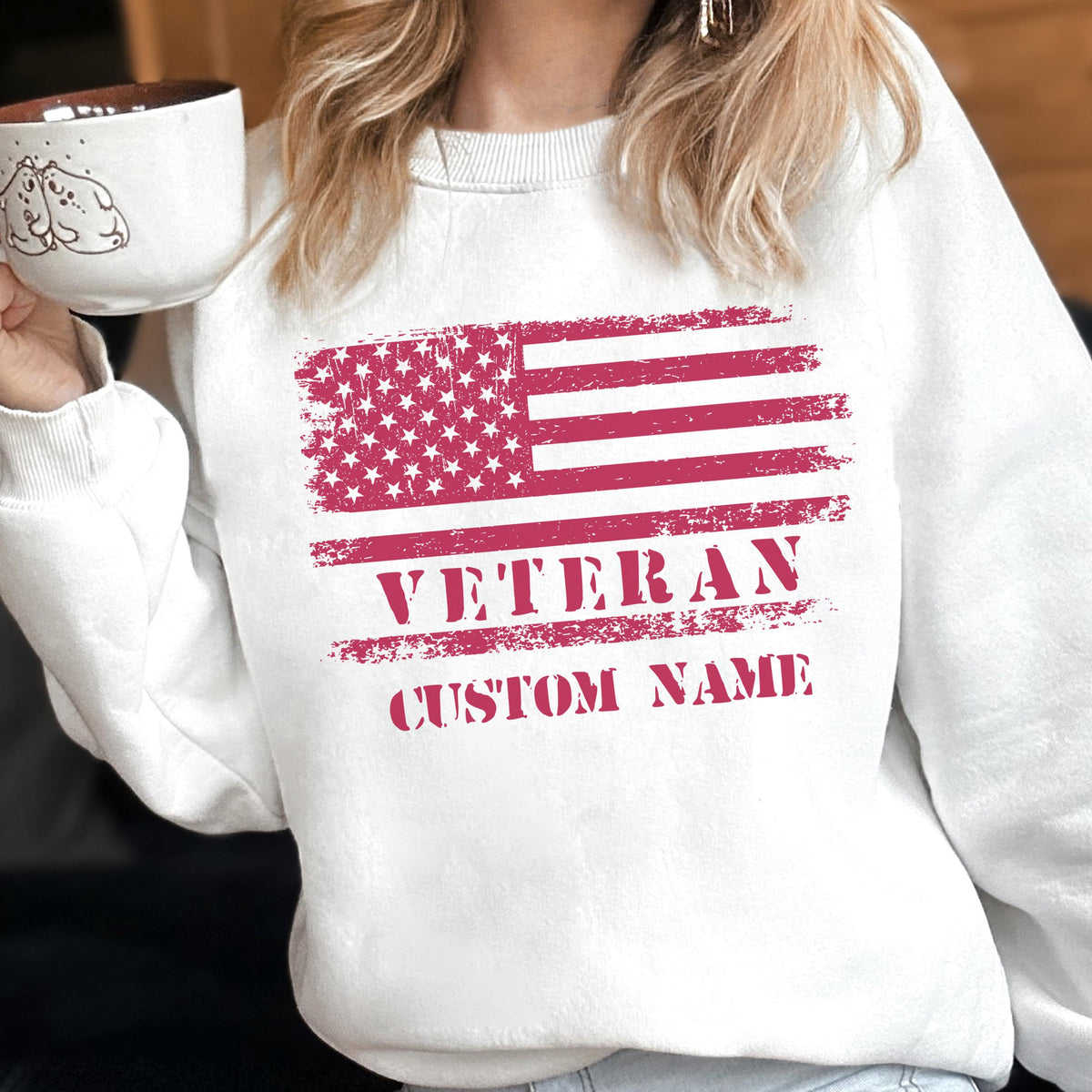 May include: White sweatshirt featuring a distressed American flag design in red. The word "VETERAN" is printed below the flag, with "CUSTOM NAME" underneath. The sweatshirt is a casual style.