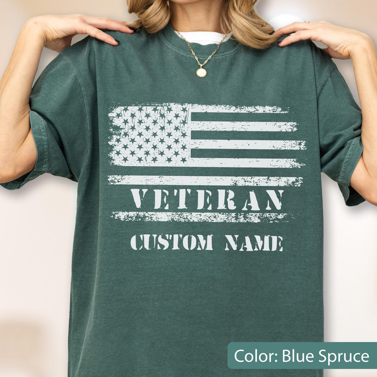 May include: A blue spruce short-sleeve t-shirt featuring a distressed white graphic of the American flag. Below the flag, the word VETERAN is printed in a bold, distressed white font, followed by the text CUSTOM NAME in the same style.