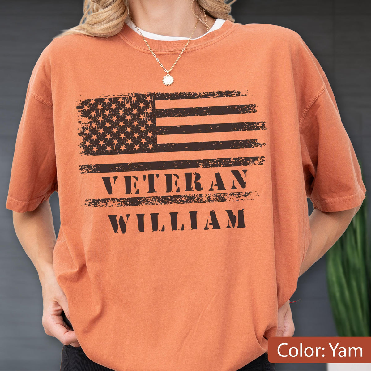 May include: A yam-colored short-sleeve t-shirt featuring a distressed black graphic of the American flag. Below the flag, the text reads VETERAN WILLIAM in a bold, distressed black font. The shirt has a crew neckline and a relaxed fit.