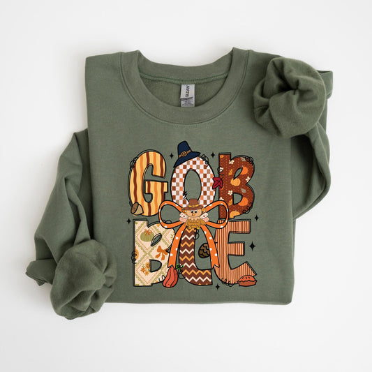 May include: Olive green sweatshirt with the words "GOB BAE" in a fall-themed design. The letters are decorated with patterns, a scarecrow, and fall leaves. The sweatshirt has long sleeves and a crew neck.