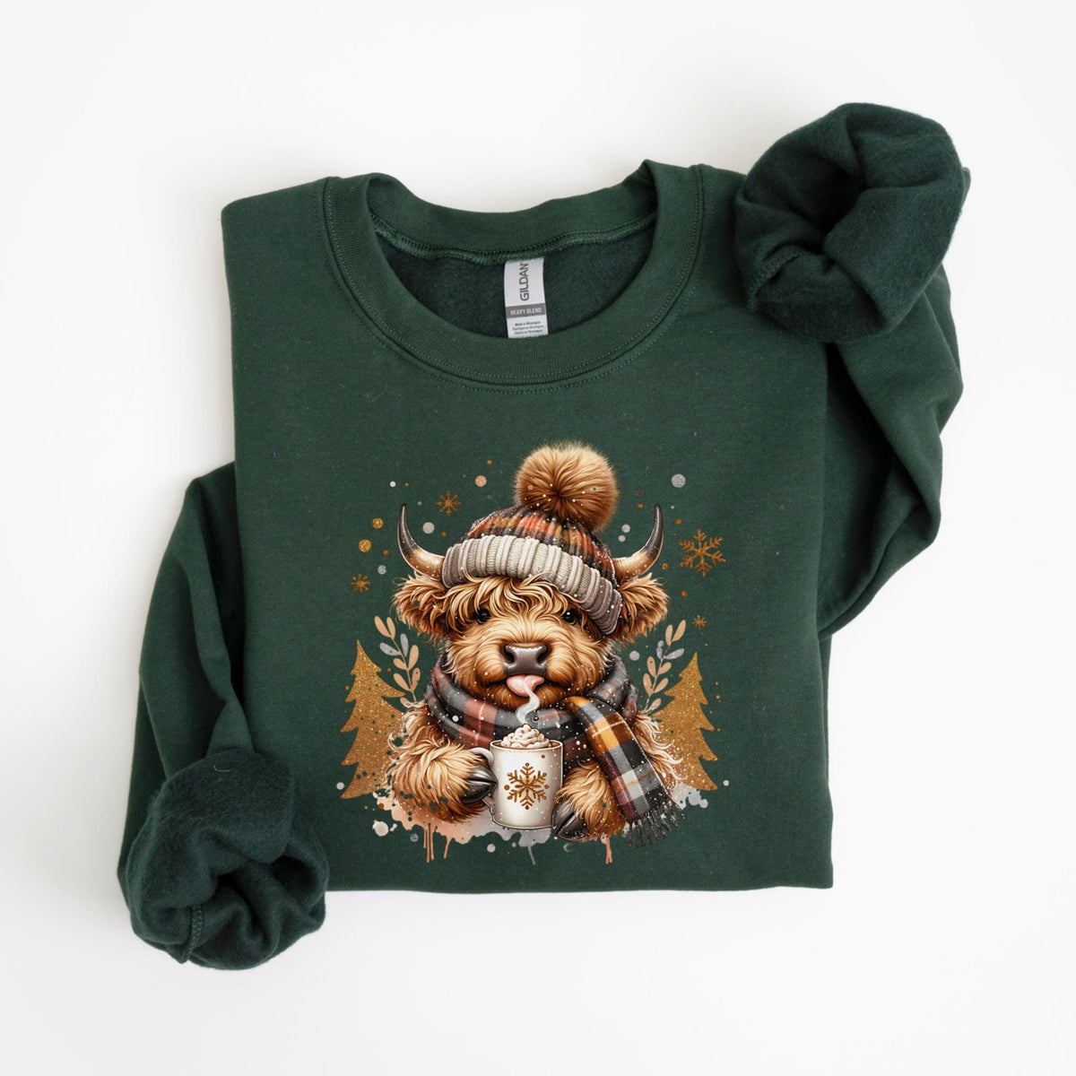 May include: A dark green sweatshirt featuring a Highland cow illustration. The cow is wearing a plaid hat and scarf, holding a mug of hot chocolate. The design includes snowflakes and gold accents, creating a cozy, winter theme.