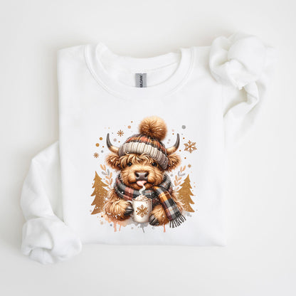 May include: White sweatshirt featuring a watercolor illustration of a Highland cow wearing a plaid hat and scarf. The cow is holding a mug with a snowflake design. The design includes snowflakes and gold Christmas trees.