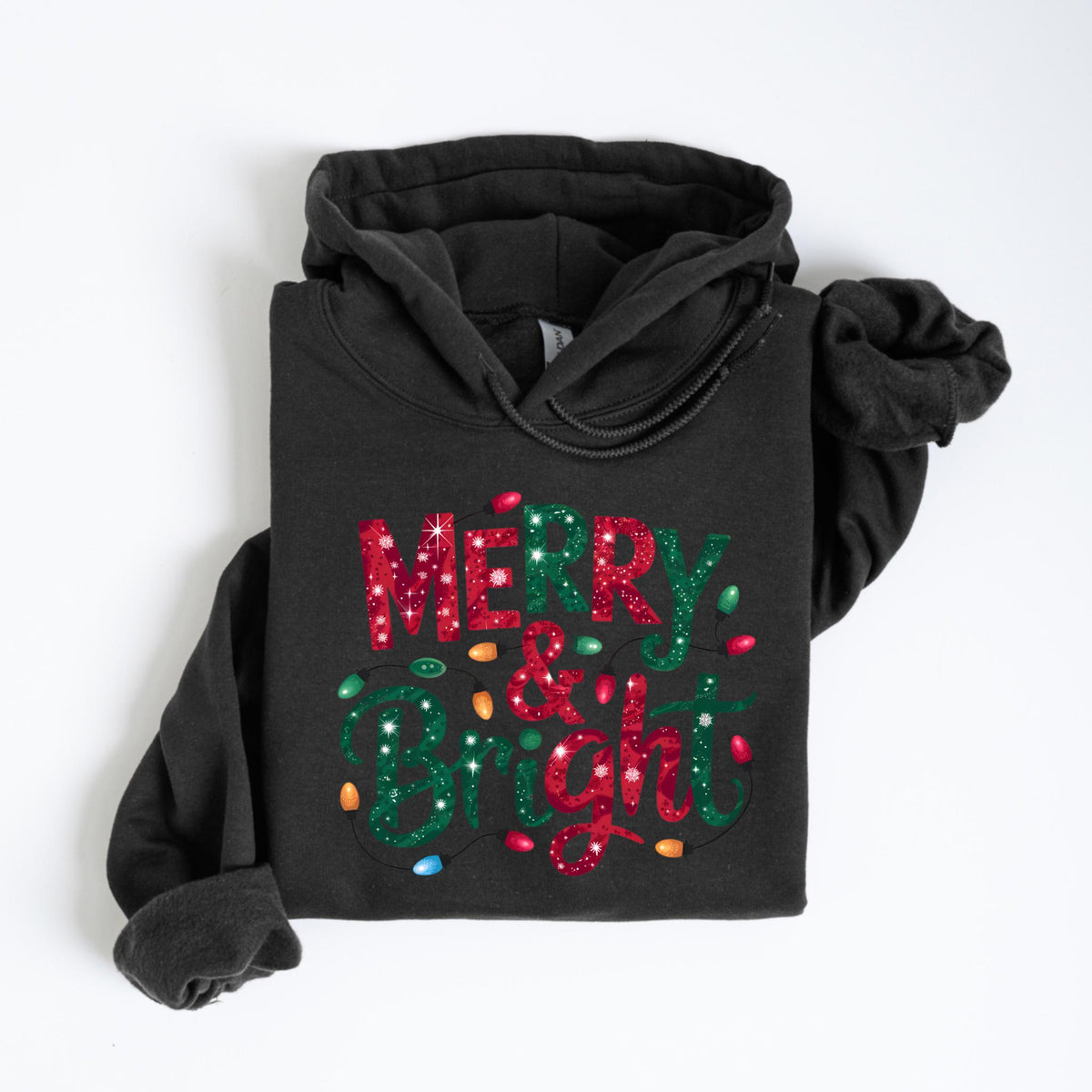 May include: A dark gray hoodie with the words "MERRY & BRIGHT" in red and green glitter lettering. The design includes colorful string lights. The hoodie is folded neatly on a white surface.