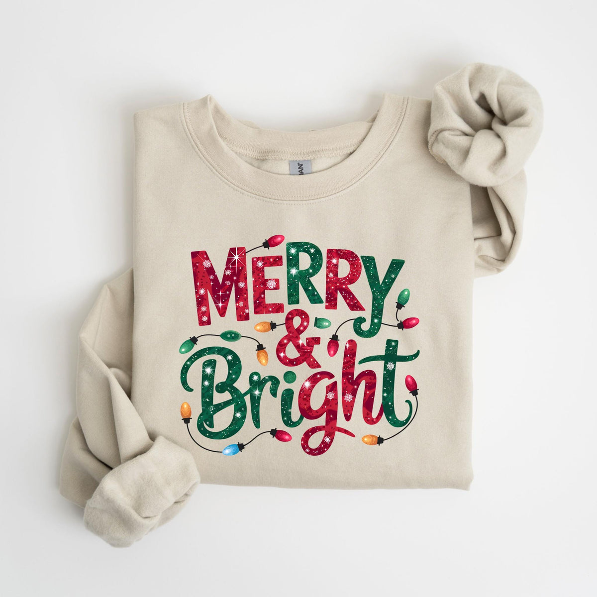May include: A beige sweatshirt with the words "MERRY & BRIGHT" in red and green, decorated with colorful Christmas lights. The sweatshirt is folded, with one sleeve rolled up.