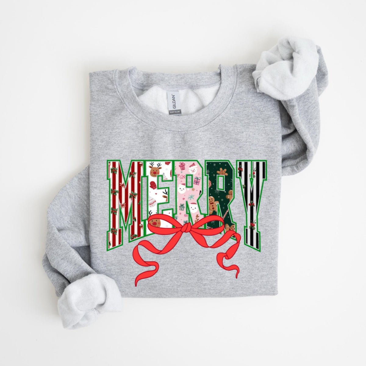 May include: A light gray sweatshirt with the word "MERRY" in a festive design. The letters are filled with holiday patterns, including reindeer, gifts, and gingerbread men. A large red bow is at the bottom of the word.