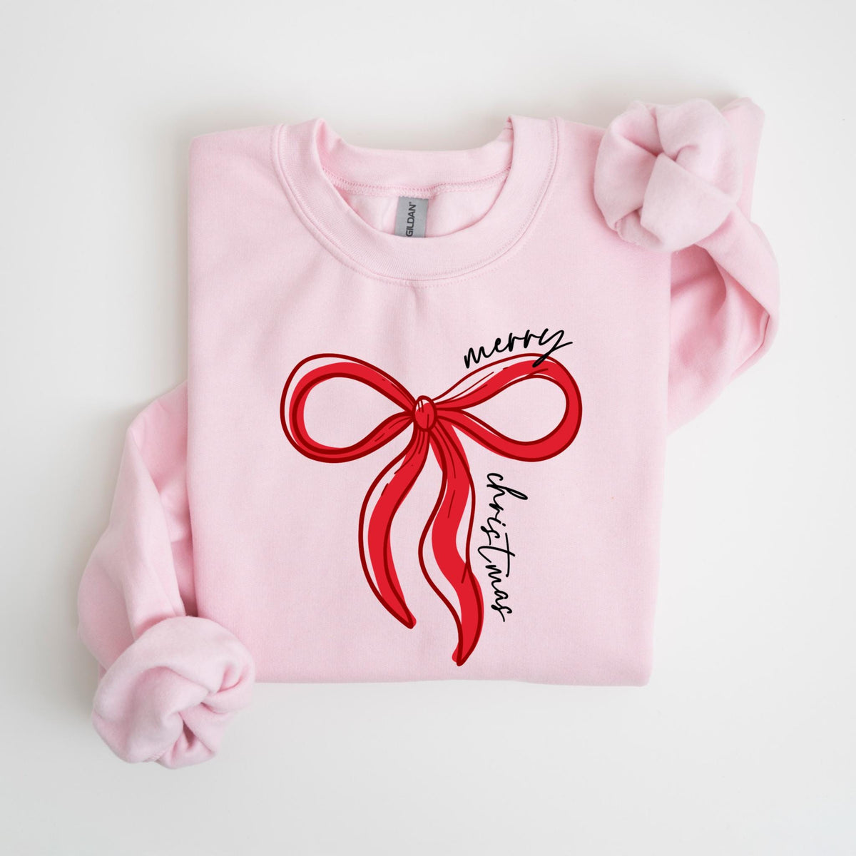 May include: A light pink sweatshirt featuring a red bow design with the words "merry christmas" in black script. The bow is a simple, elegant illustration. The sweatshirt has long sleeves and a crew neck.