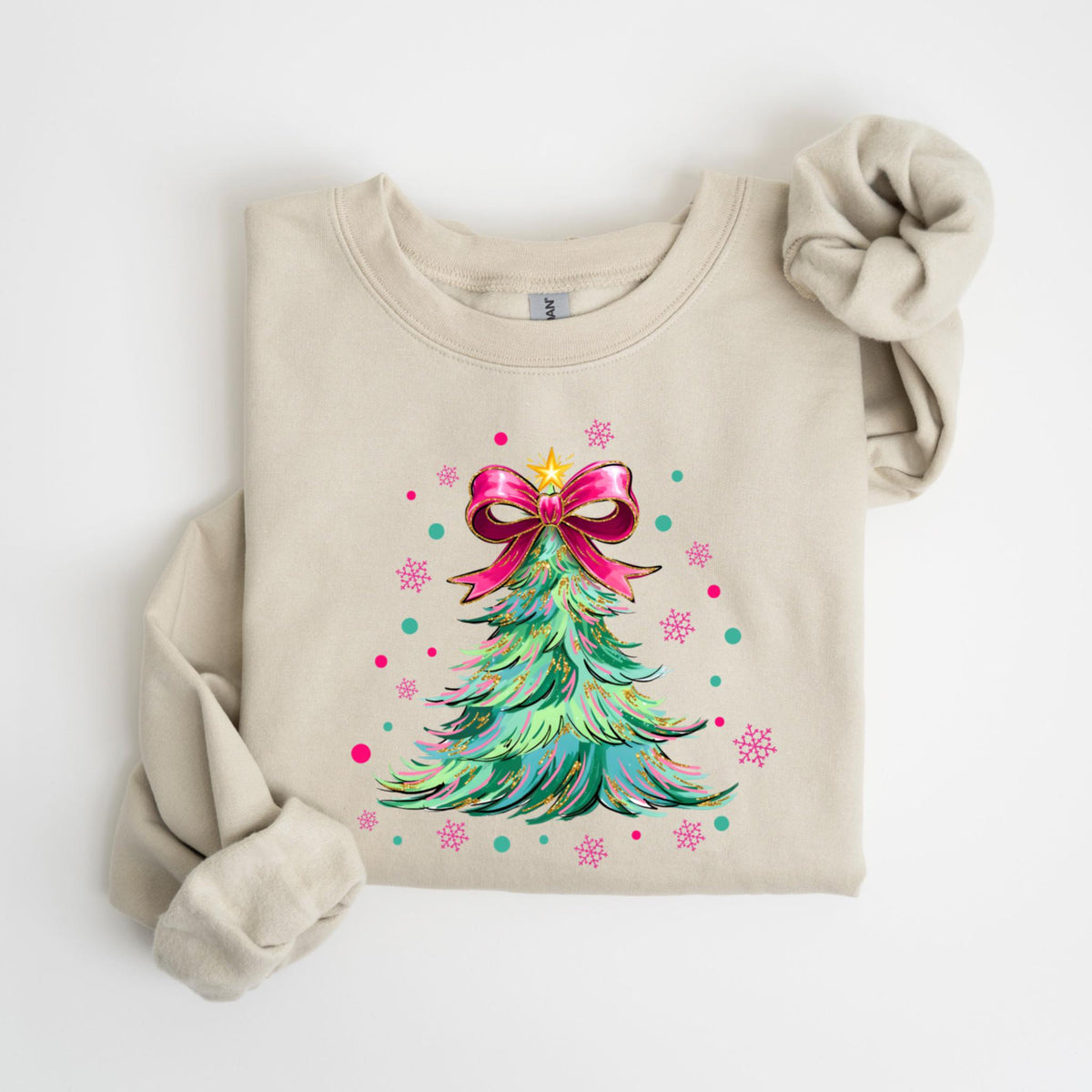 May include: A beige sweatshirt featuring a colorful Christmas tree design. The tree is decorated with a pink bow, a gold star, and pink and teal accents. The sleeves are rolled up, and the sweatshirt is laid flat.