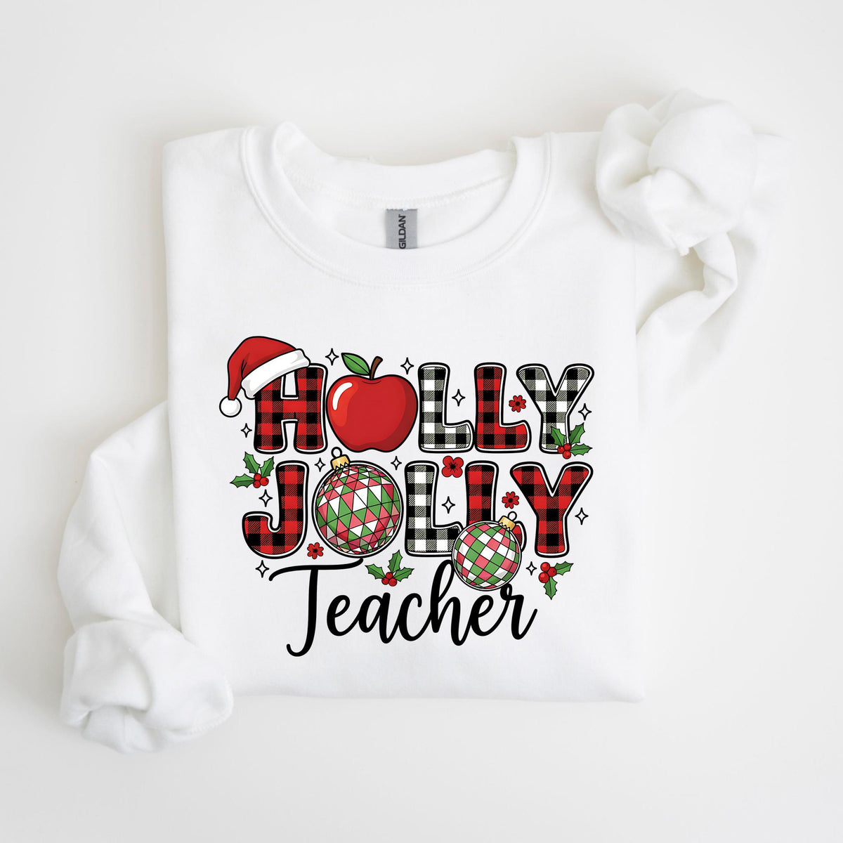 May include: White sweatshirt with a festive graphic. The design features the words "HOLLY JOLLY Teacher" in a mix of red and black plaid letters, a Santa hat, a red apple, and Christmas ornaments. The overall theme is holiday-themed.