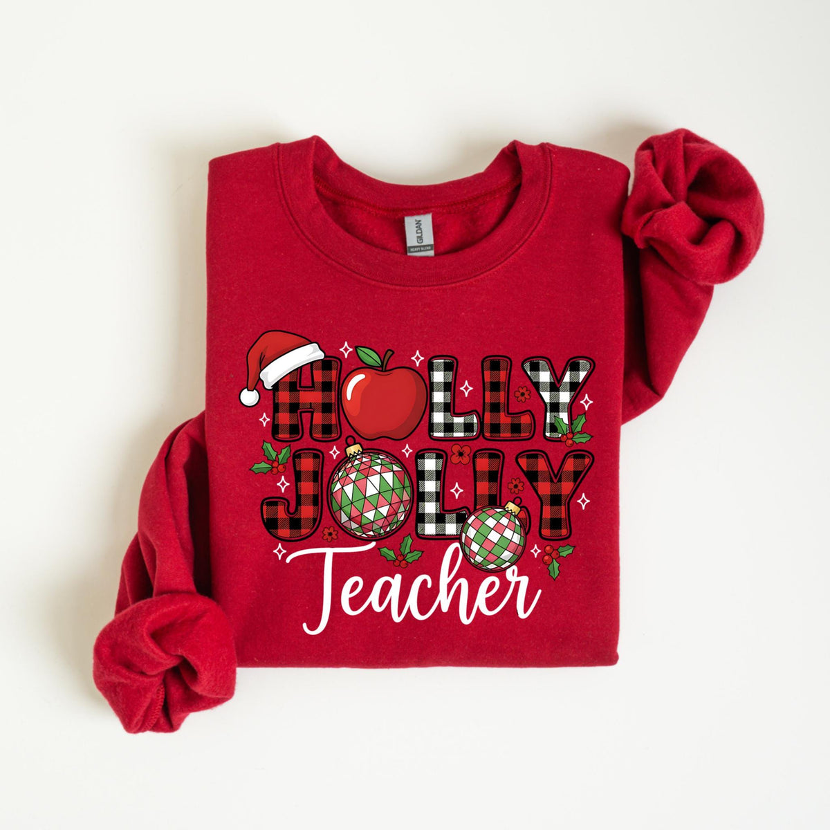 May include: A red sweatshirt with the words "HOLLY JOLLY Teacher" in a festive design. The design includes a Santa hat, an apple, and Christmas ornaments. The letters are in a mix of plaid and solid colors.