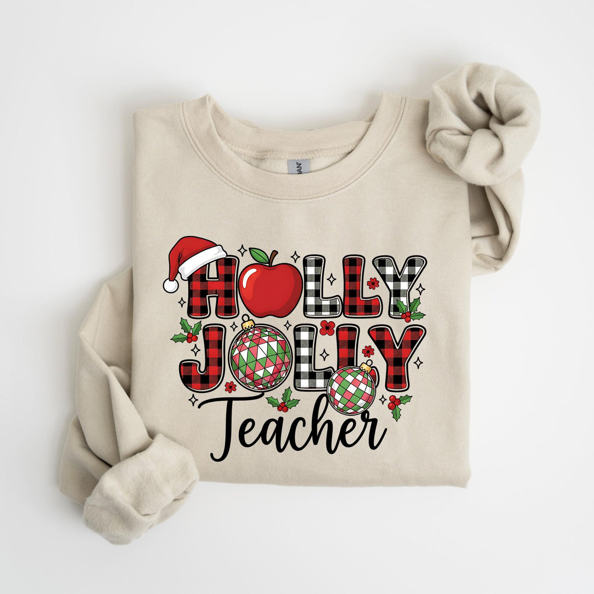 May include: Beige sweatshirt with the words "HOLLY JOLLY Teacher" in a festive design. The letters are a mix of red and black buffalo plaid, with a Santa hat, apple, and Christmas ornaments. The sweatshirt has long sleeves and a crew neck.