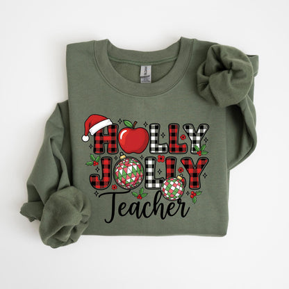 May include: An olive green sweatshirt with a festive design. The design includes the words "HOLLY JOLLY Teacher" in a mix of plaid, red, and black lettering, along with a Santa hat, apple, and Christmas ornaments. A seasonal apparel item.