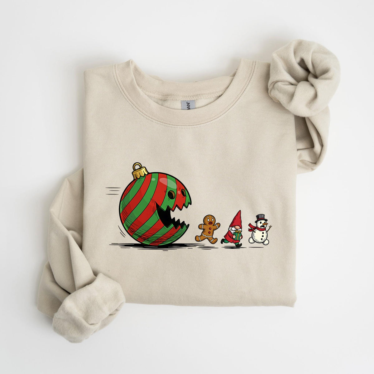 May include: A beige sweatshirt featuring a whimsical Christmas-themed graphic. The design depicts a red and green striped ornament with a bite taken out of it, chasing a gingerbread man, a gnome, and a snowman. The sweatshirt has long sleeves and a crew neck.