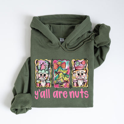 May include: Olive green hoodie with a graphic featuring three colorful nutcrackers and the text "y'all are nuts" in pink. The nutcrackers have ornate hats and bow ties. The hoodie has a drawstring and a front pocket.