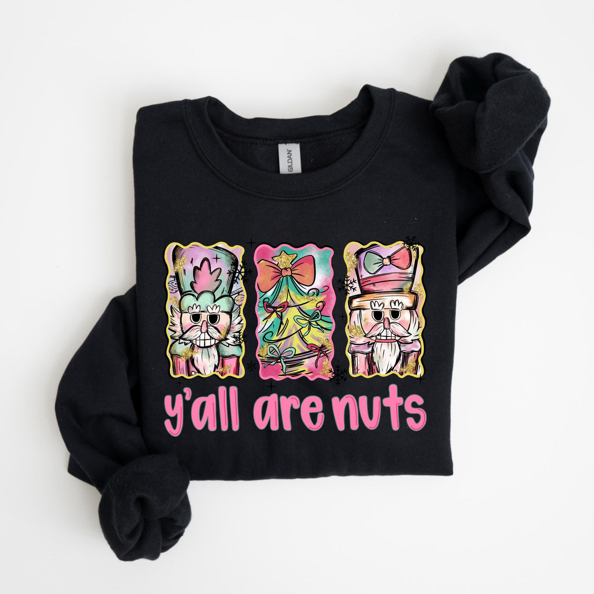 May include: Black sweatshirt with a colorful graphic of three nutcrackers and a Christmas tree. The text "y'all are nuts" is printed in pink below the graphic. The sweatshirt is folded.