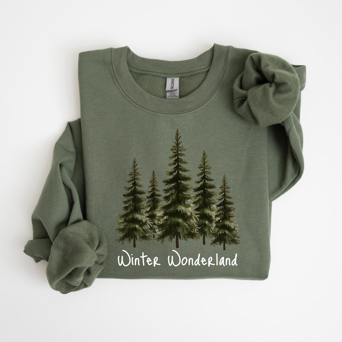 May include: An olive green sweatshirt featuring a watercolor illustration of five evergreen trees. The words "Winter Wonderland" are printed in white script below the trees. The sweatshirt has long sleeves and a crew neck.