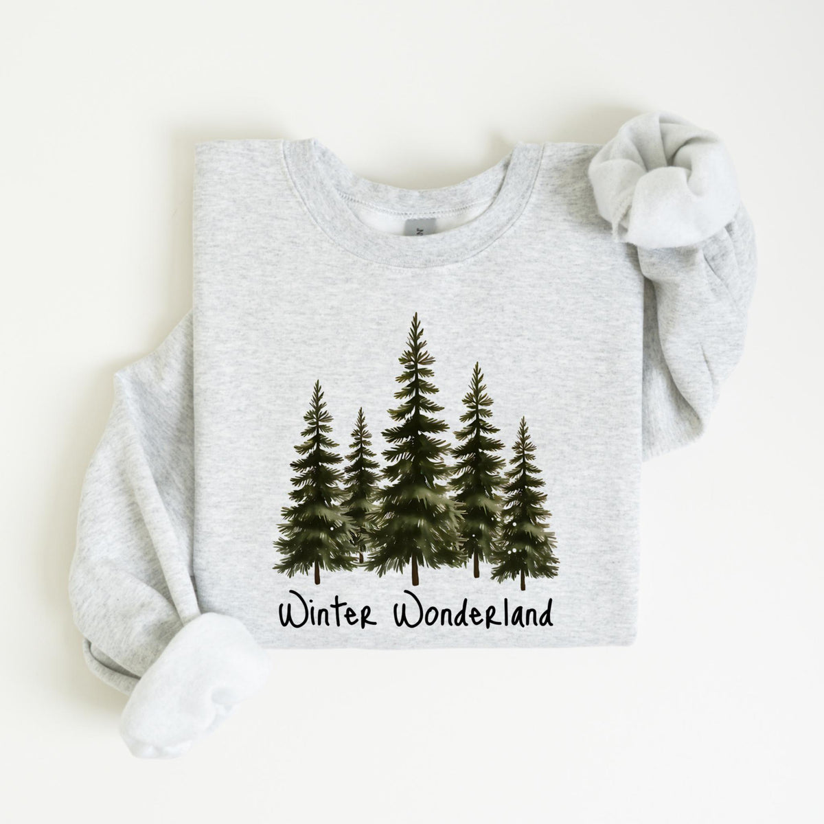 May include: A light gray sweatshirt featuring a watercolor design of five evergreen trees. Below the trees is the text "Winter Wonderland" in a handwritten style. The sweatshirt has a crew neck and long sleeves.