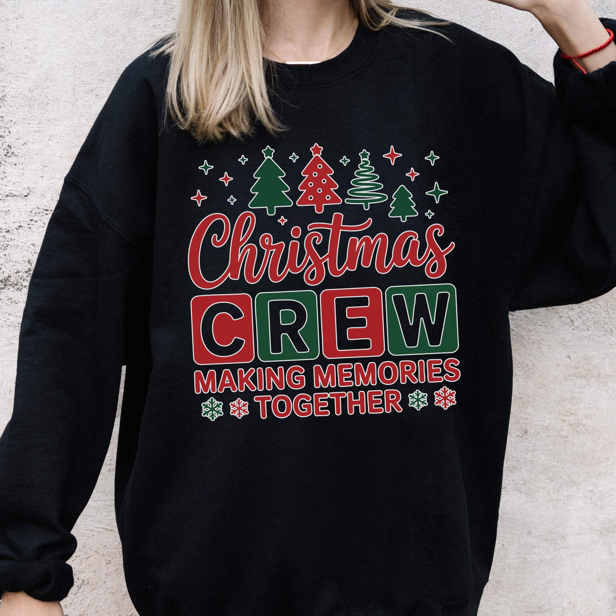 May include: A black crewneck sweatshirt featuring a graphic print with the text Christmas CREW MAKING MEMORIES TOGETHER. The design includes red and green block letters, stylized Christmas trees, and snowflake icons in red and green.