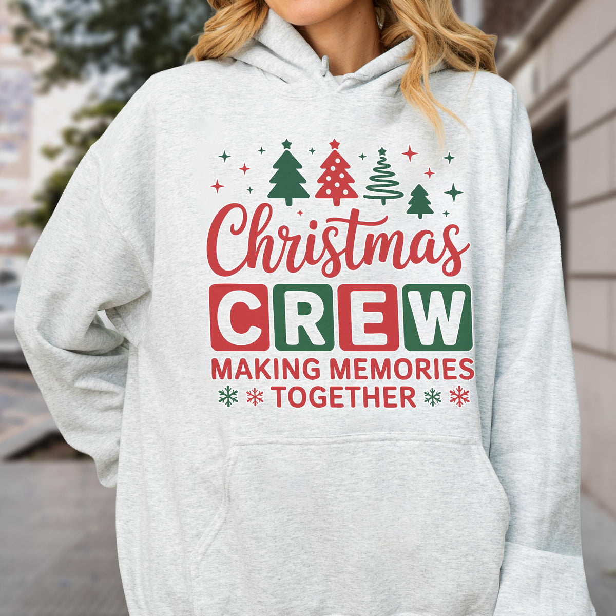 May include: A light gray hooded sweatshirt featuring a graphic print with the text "Christmas CREW MAKING MEMORIES TOGETHER" in red and green. The design includes illustrations of four pine trees and small star and snowflake accents.