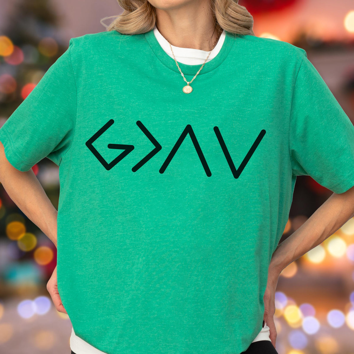 May include: A bright green short-sleeved t-shirt featuring a black graphic print on the chest. The design consists of the mathematical symbols for greater than, less than, and equal to, arranged to read as G > < V, representing God is greater than the highs and lows.