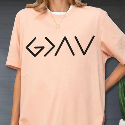 May include: A peach-colored short-sleeve t-shirt featuring the black text G > AV printed across the chest. The shirt has a crew neckline and is worn over a white undershirt, paired with a thin gold chain necklace with a small circular pendant.