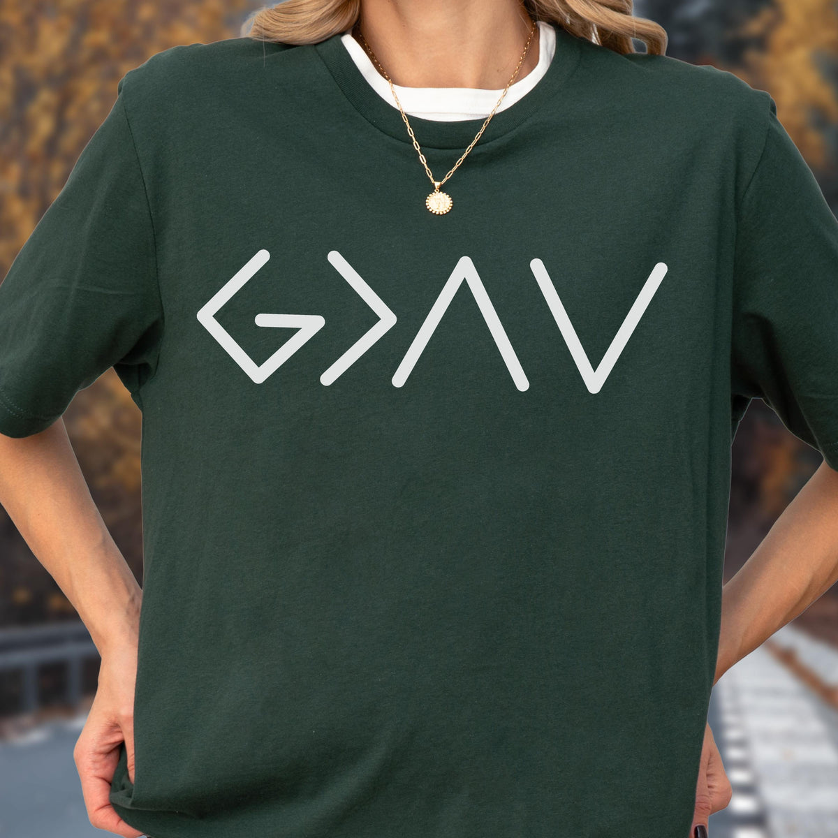 May include: A dark forest green short-sleeved t-shirt featuring a white graphic print on the chest. The design consists of the mathematical symbols G > A V in a clean, sans-serif font. The shirt has a crew neckline and a relaxed fit.