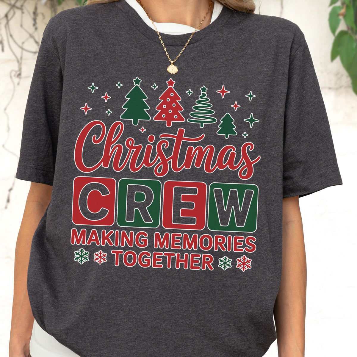 May include: A dark charcoal gray t-shirt featuring a festive graphic with the text "Christmas CREW MAKING MEMORIES TOGETHER" in red and white. The design includes green and red Christmas tree icons and small white star and snowflake accents.