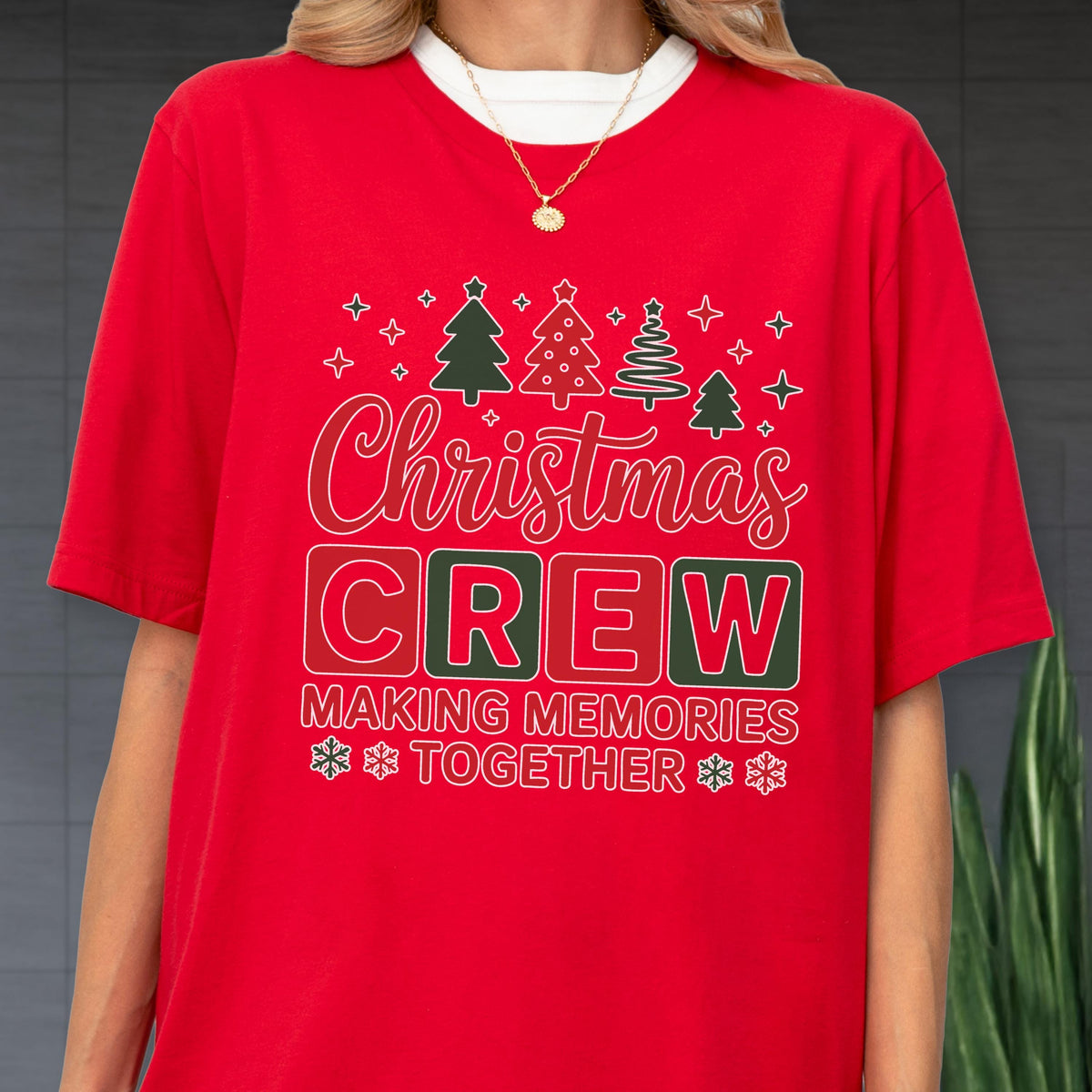 May include: A red short-sleeved t-shirt featuring a graphic with four stylized Christmas trees, the text "Christmas CREW" in white and red, and the text "MAKING MEMORIES TOGETHER" with snowflake icons. The shirt has a crew neckline.