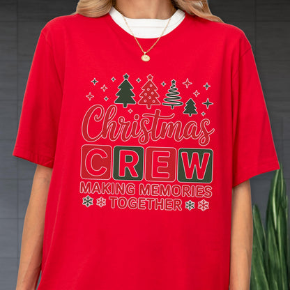 May include: A red short-sleeved t-shirt featuring a graphic with four stylized Christmas trees, the text "Christmas CREW" in white and red, and the text "MAKING MEMORIES TOGETHER" with snowflake icons. The shirt has a crew neckline.