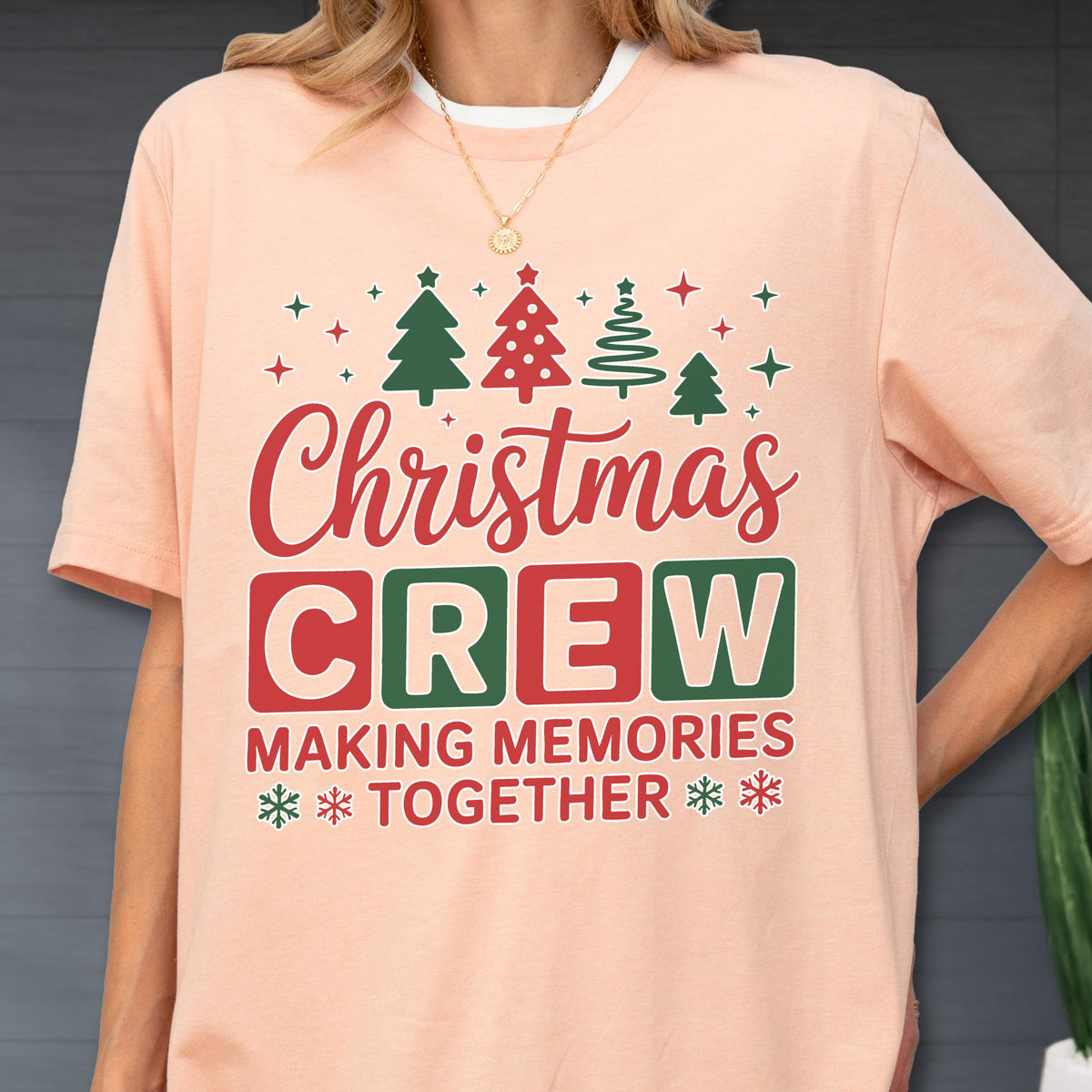 May include: A peach-colored t-shirt featuring a graphic with red and green Christmas trees, stars, and the text "Christmas CREW MAKING MEMORIES TOGETHER" in red and green block lettering, accented with small snowflake icons at the bottom.