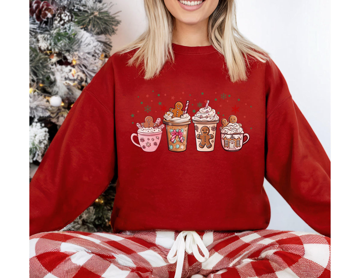 May include: A red sweatshirt featuring a festive design of four gingerbread latte cups. Each cup is decorated with whipped cream, sprinkles, and a gingerbread man. The sweatshirt is paired with red and white plaid pajama pants.