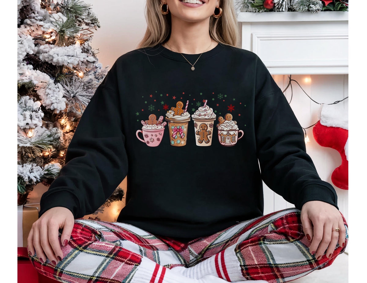 May include: Black sweatshirt featuring four festive coffee cup designs with gingerbread men, whipped cream, and candy canes. The cups are in pink, orange, and brown, with green and red accents. A cozy holiday-themed apparel item.