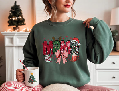 May include: A dark green sweatshirt with the word "MAMA" in a festive Christmas design. The letters are decorated with holiday elements like a Santa hat, bow, and ornaments. A white mug with a Christmas tree design is held in the hand.