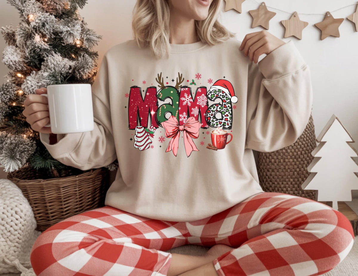 May include: Beige sweatshirt with the word "MAMA" in a Christmas-themed design. The letters are red and green with festive accents like a Santa hat, bow, and Christmas tree. The person is wearing red and white plaid pants and holding a white mug.