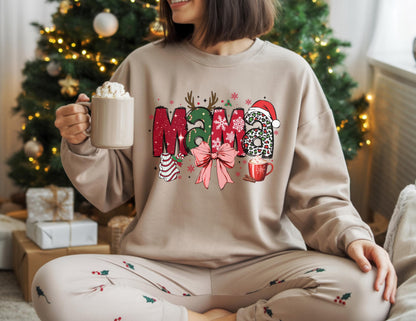May include: Beige sweatshirt with the word "Mama" in a Christmas-themed design. The letters are decorated with red, green, and leopard print patterns, a bow, and a Santa hat. A mug of whipped cream is held in the hand.