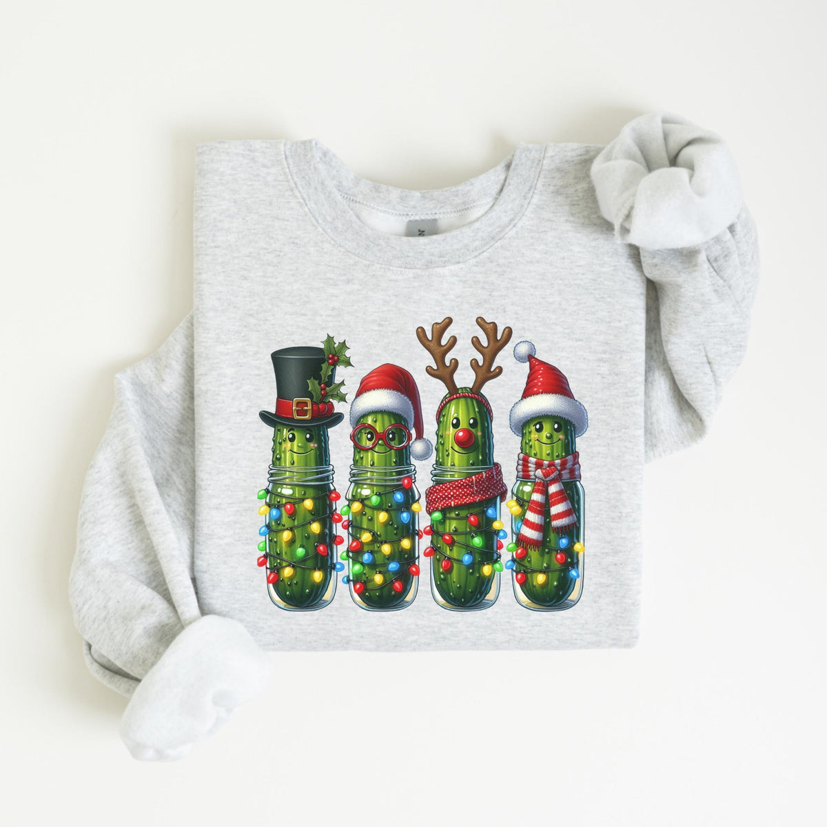 May include: A light gray sweatshirt featuring a festive graphic of four pickles in mason jars, each adorned with Christmas decorations. One pickle wears a top hat, another a Santa hat, another reindeer antlers, and the last a Santa hat and scarf.