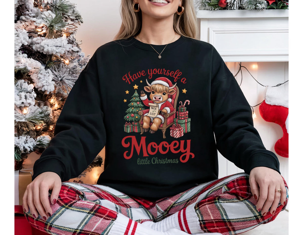 May include: Black crewneck sweatshirt with a Christmas graphic. The graphic features a cartoon cow wearing a Santa hat, sitting in a chair, and holding a list. Text reads "Have yourself a Mooey little Christmas."