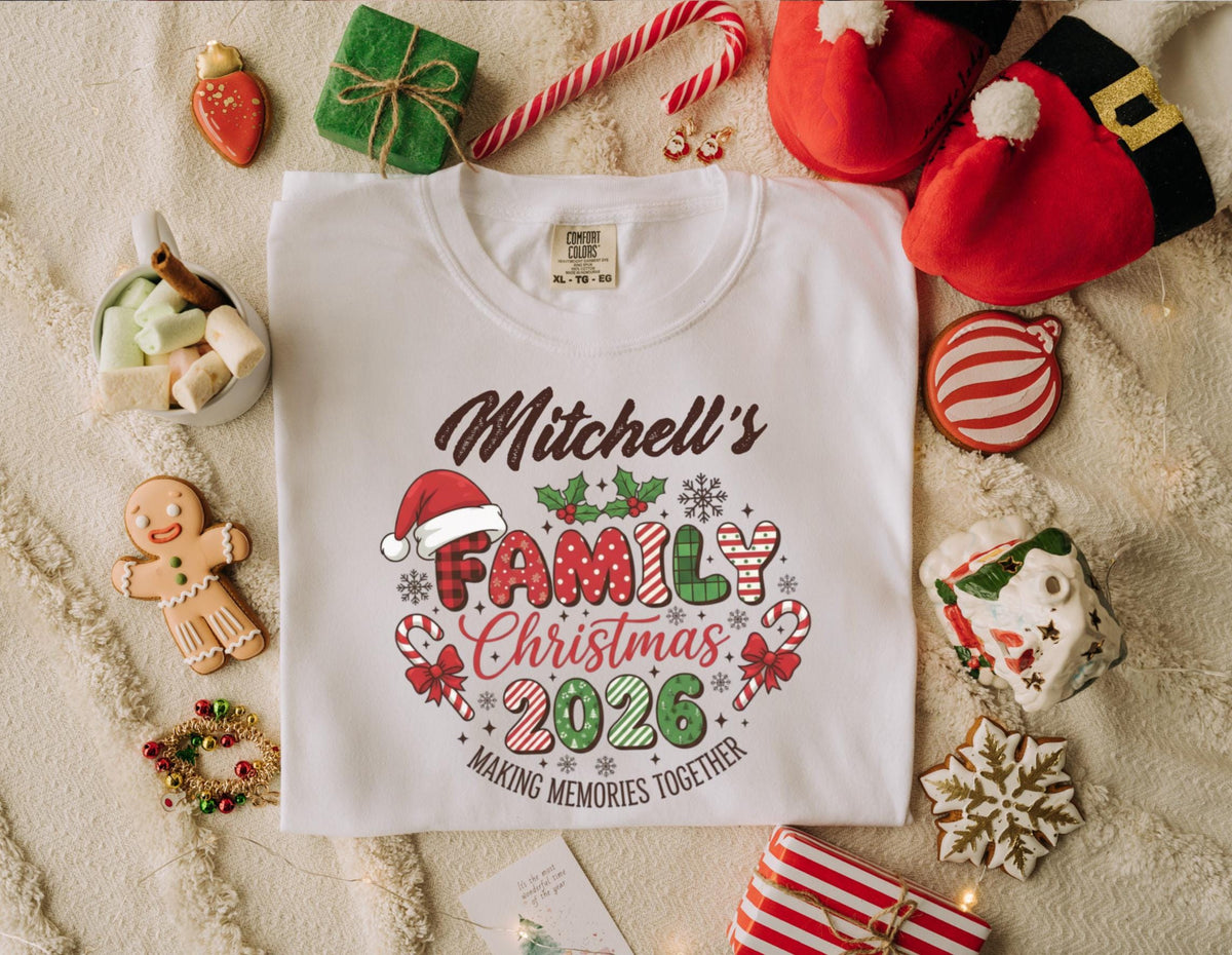 May include: White t-shirt with a Christmas-themed graphic. The design includes the text "Mitchell's Family Christmas 2026" with a Santa hat, holly, and candy canes. The shirt is surrounded by festive decorations like gingerbread cookies and wrapped gifts.