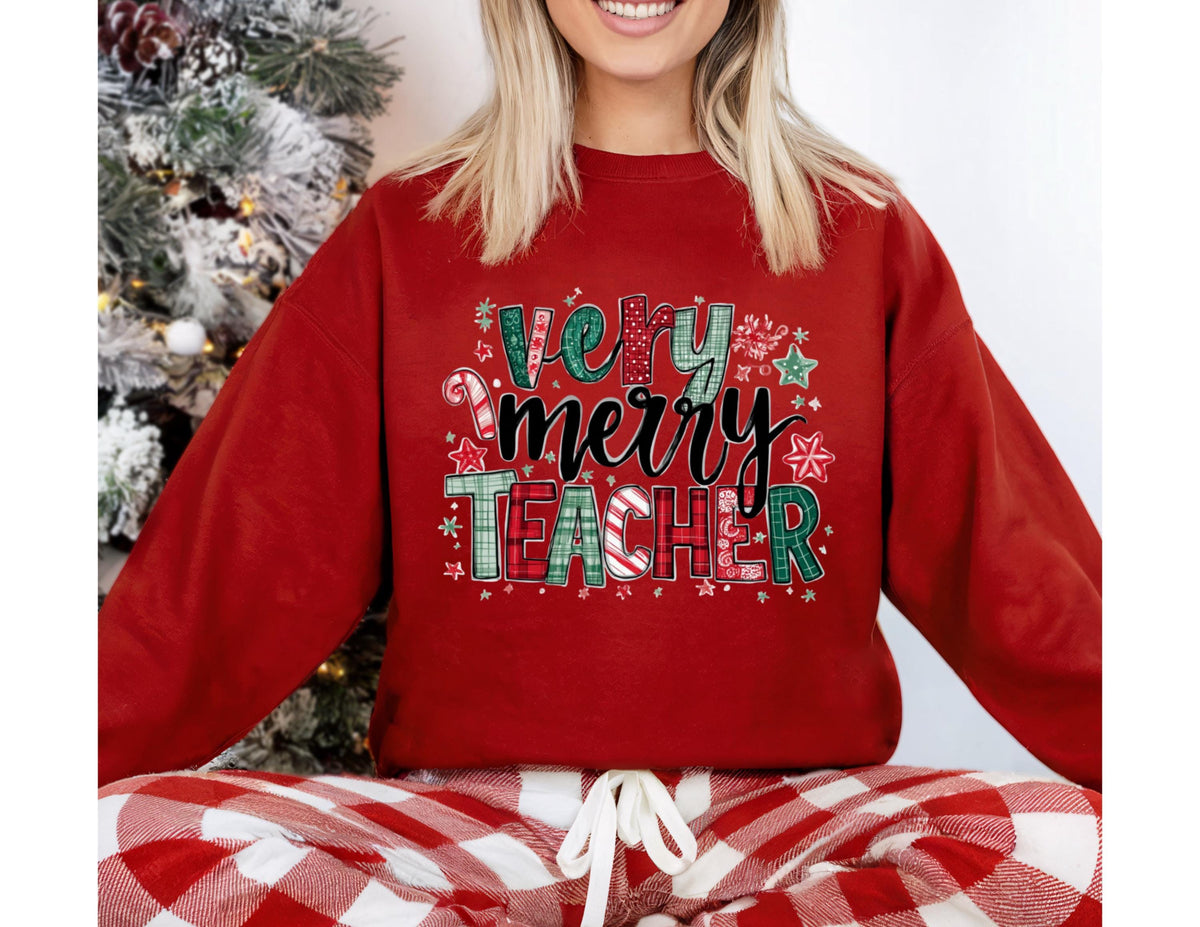 May include: A red sweatshirt with the text "Very Merry Teacher" in a festive design. The text incorporates candy canes, snowflakes, and stars. The sweatshirt is paired with red and white plaid pajama pants.