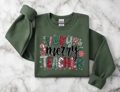 May include: An olive green sweatshirt with the words "Very Merry Teacher" in a festive design. The text features a mix of patterns, including plaid, candy canes, and stars, in red, green, and white. The sweatshirt has a crew neck and long sleeves.